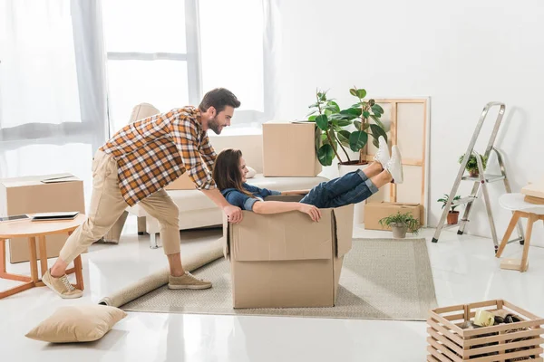 Vista laterale di coppia divertirsi con scatola di cartone a casa nuova, trasferirsi concetto di casa — Foto stock