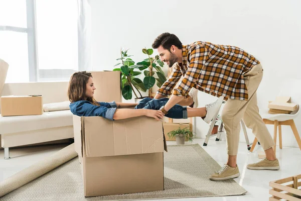 Side view of couple having fun with cardboard box at new house, moving home concept — Stock Photo