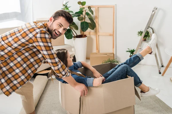 Vista lateral do casal se divertindo com caixa de papelão na nova casa, movendo-se para casa conceito — Fotografia de Stock