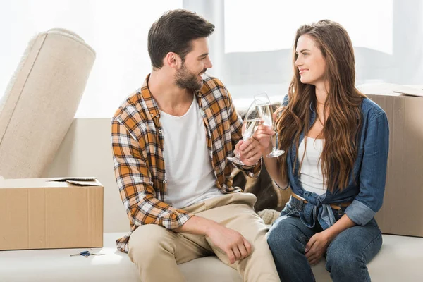 Couple in love clinking glasses of champagne at new house with cardboard boxes, moving home concept — Stock Photo