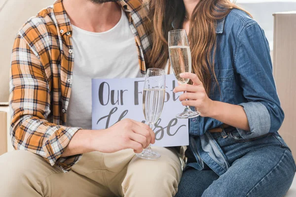 Partial view of couple with glasses of champagne and our first house card, moving home concept — Stock Photo