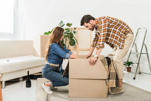 Side view of couple unpacking cardboard boxes together at new home, moving home concept — Stock Photo