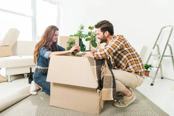 Side view of young couple unpacking cardboard boxes together at new home, moving home concept — Stock Photo