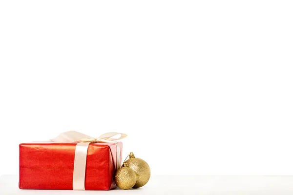 Caja de regalo envuelta por cinta y adornos de Navidad dorados sobre fondo blanco - foto de stock