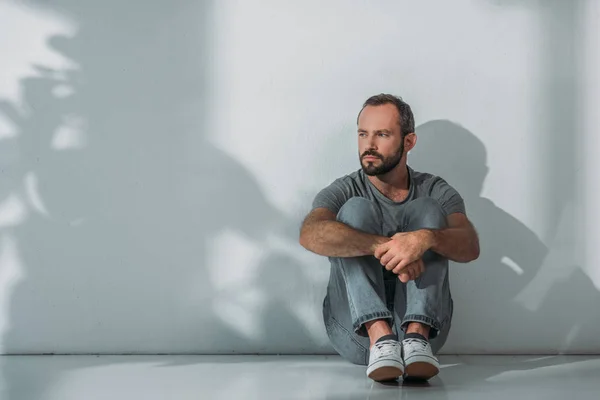 Full length view of depressed bearded middle aged man sitting on floor and looking away — Stock Photo