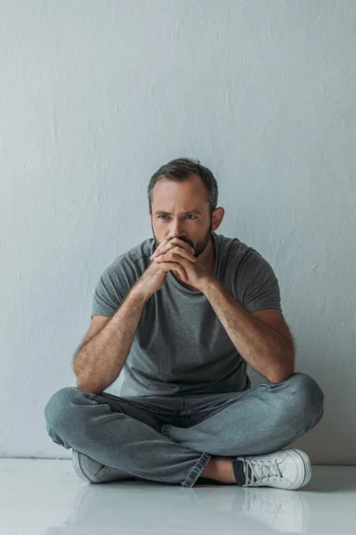 Full length view of unhappy bearded man sitting on floor and looking away — Stock Photo