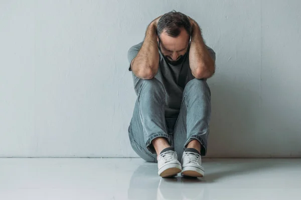 Full length view of frustrated middle aged man sitting with hands behind head on floor — Stock Photo