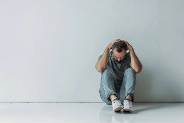 Ganzkörperansicht eines verängstigten depressiven Mannes, der mit den Händen hinter dem Kopf auf dem Boden sitzt — Stockfoto