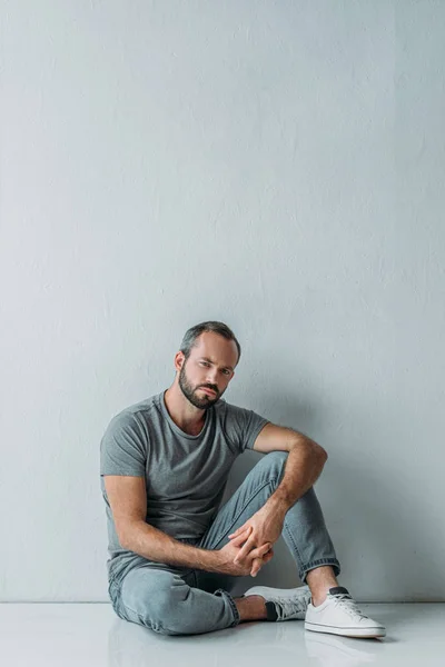 Full length view of sad mid adult man sitting on floor and looking at camera — Stock Photo