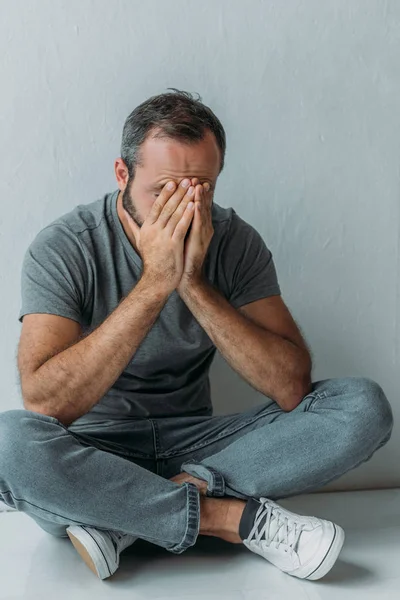 Vista de ángulo alto del hombre de mediana edad estresado sentado con las manos en la cara - foto de stock