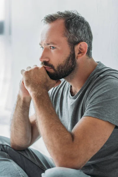 Sad handsome bearded man sitting with hands on chin and looking away — Stock Photo