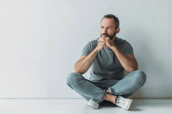 Unhappy bearded man sitting in floor and looking away — Stock Photo