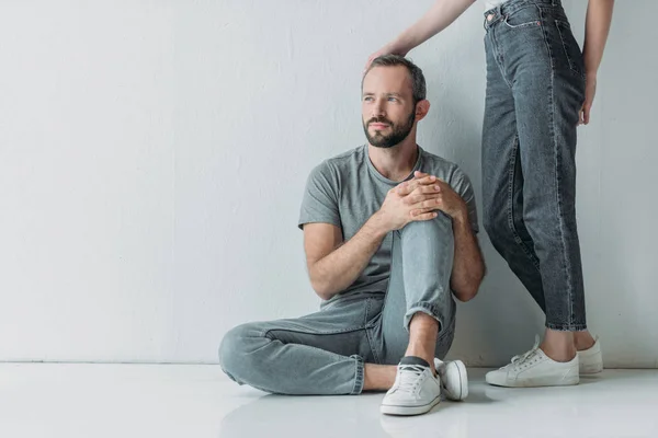 Cropped shot of young woman touching frustrated bearded man sitting on floor and looking away — Stock Photo