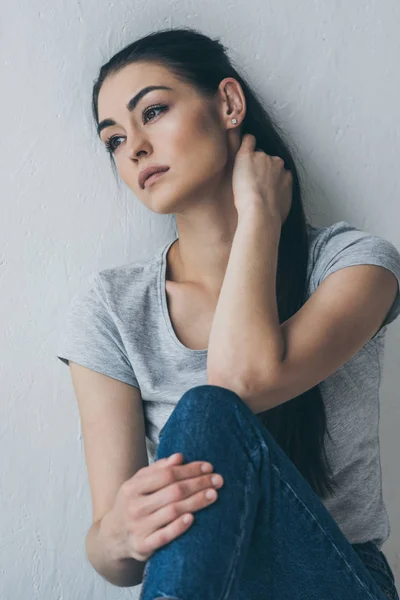 Depressiva attraente ragazza bruna seduta e guardando lontano sul grigio — Foto stock