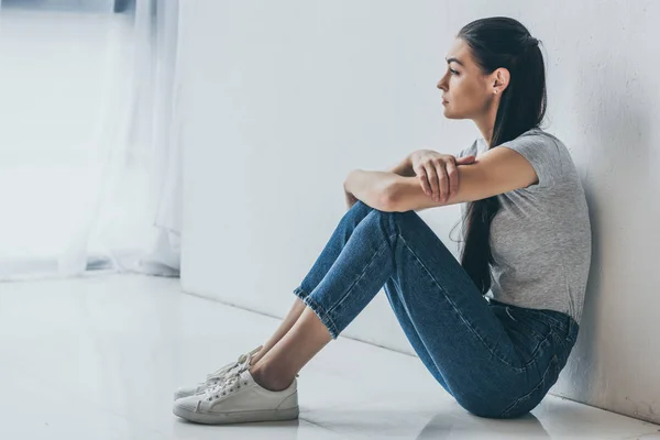 Vista laterale di bella ragazza bruna sconvolta seduta e distogliendo lo sguardo — Foto stock