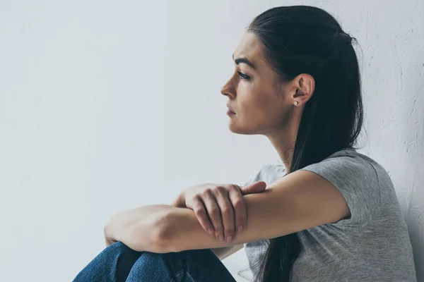 Side view of beautiful frustrated brunette girl sitting and looking away on grey — Stock Photo