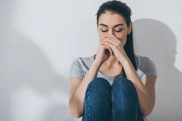 Trauriges gestresstes Mädchen sitzt mit geschlossenen Augen an grauer Wand — Stockfoto