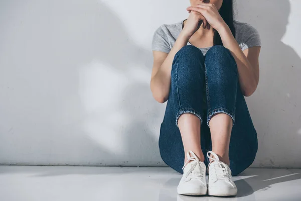Tiro recortado de mulher jovem deprimida sentado no chão perto da parede cinza — Fotografia de Stock