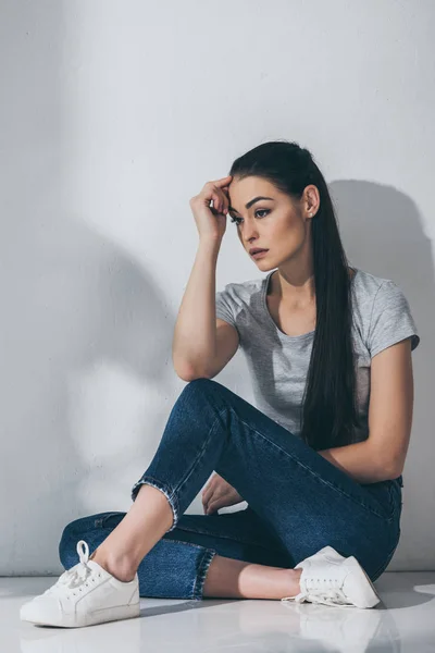 Stressé jeune femme assise sur le sol avec la main sur le front et regardant loin — Photo de stock