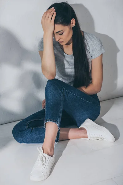 Hochwinkelaufnahme einer gestressten jungen Frau, die mit der Hand auf der Stirn auf dem Boden sitzt — Stockfoto