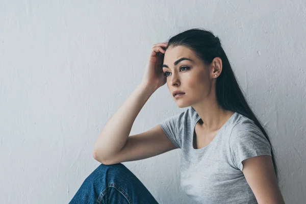 Upset beautiful brunette girl sitting and looking away on grey — Stock Photo