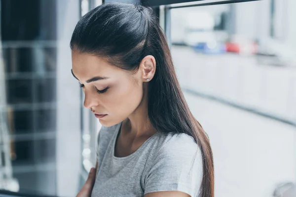 Portrait de jeune femme triste debout les yeux fermés près de la fenêtre — Photo de stock