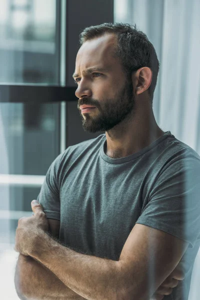 Ernster bärtiger Mann mittleren Alters steht mit verschränkten Armen und schaut weg — Stockfoto