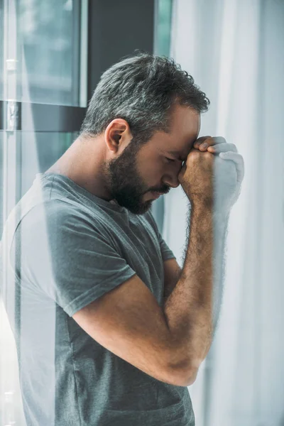 Вид збоку депресивний розчарований бородатий чоловік стоїть біля вікна — стокове фото