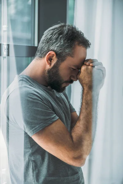 Vue latérale de l'homme barbu frustré déprimé debout près de la fenêtre — Photo de stock