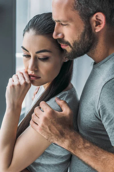 Seitenansicht eines bärtigen Mannes, der eine aufgebrachte junge Frau umarmt und unterstützt — Stockfoto