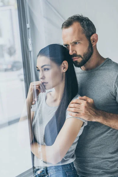 Upset couple standing together and looking at window — Stock Photo