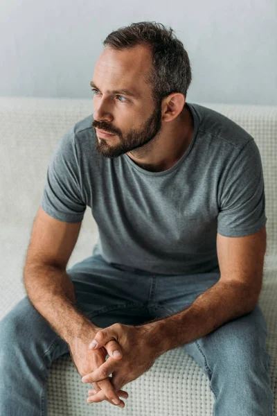 Bärtiger, nachdenklicher Mann mittleren Alters sitzt auf der Couch und schaut weg — Stockfoto