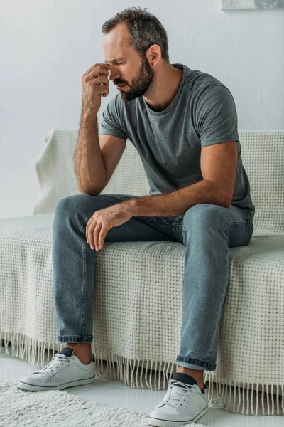 Sad bearded man sitting on couch and rubbing nose bridge — Stock Photo