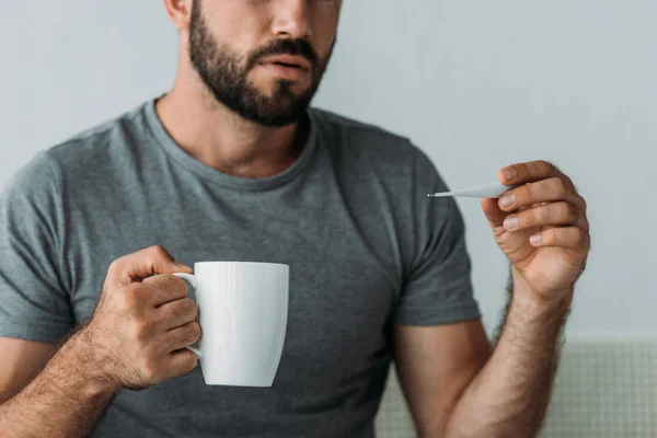 Обрізаний знімок хворого бородатого чоловіка, який тримає термометр і чашку — стокове фото