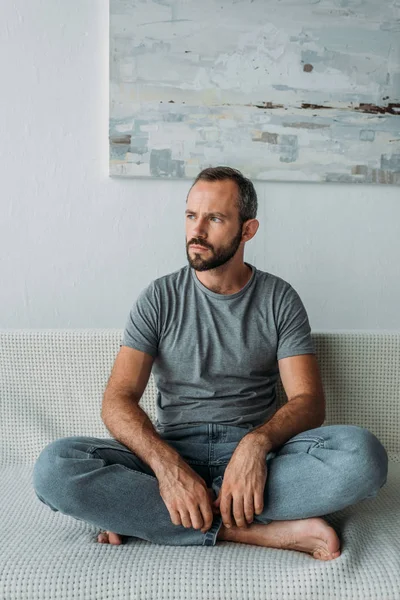 Pensive bearded mid adult man sitting on couch and looking away — Stock Photo