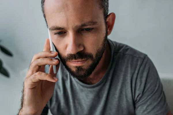 Bouleversé homme barbu parler par smartphone et regarder vers le bas — Photo de stock