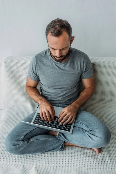 High angle view of unhappy bearded man sitting on couch and using laptop — Stock Photo