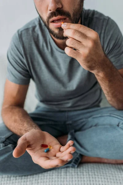 Recortado disparo de barbudo hombre de mediana edad sentado en el sofá y tomar pastillas - foto de stock