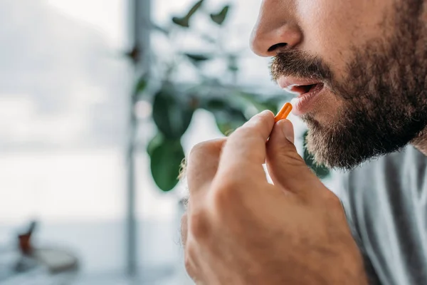 Обрізаний знімок бородатого чоловіка тримає таблетку біля рота — стокове фото