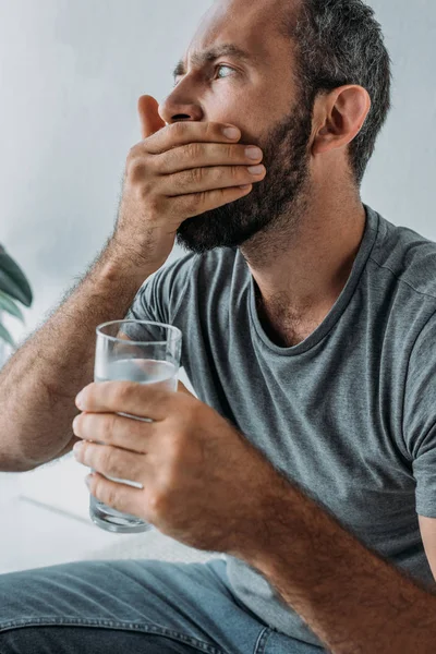 Homme barbu tenant un verre d'eau et prenant des médicaments — Photo de stock