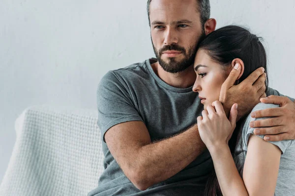 Bearded man supporting and hugging depressed woman sitting on couch — Stock Photo
