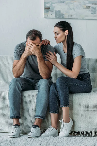 Young woman supporting sad boyfriend sitting on couch with hands on face — Stock Photo