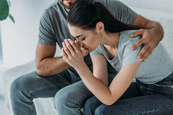 Cropped shot of man supporting upset girlfriend while sitting together on couch — Stock Photo