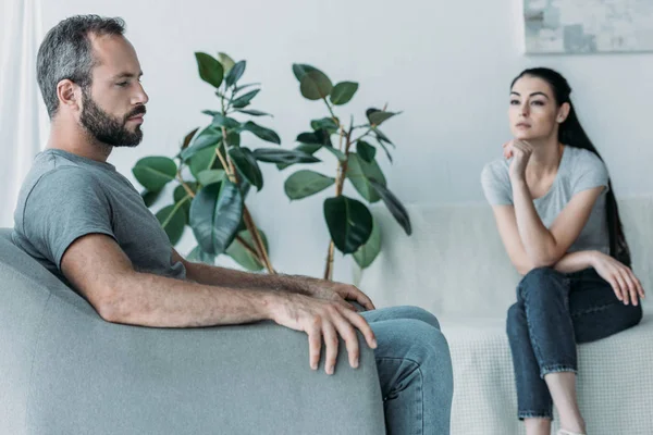 Chateado barbudo homem sentado no poltrona e frustrado mulher sentado no sofá, relacionamento dificuldades conceito — Fotografia de Stock