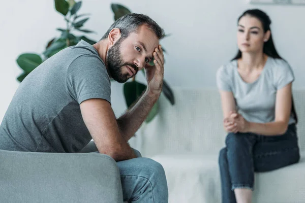 Upset middle aged man sitting on couch and girlfriend sitting behind — Stock Photo