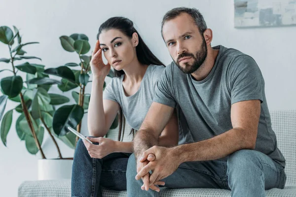 Triste pareja estresada con prueba de embarazo sentado y mirando a la cámara - foto de stock