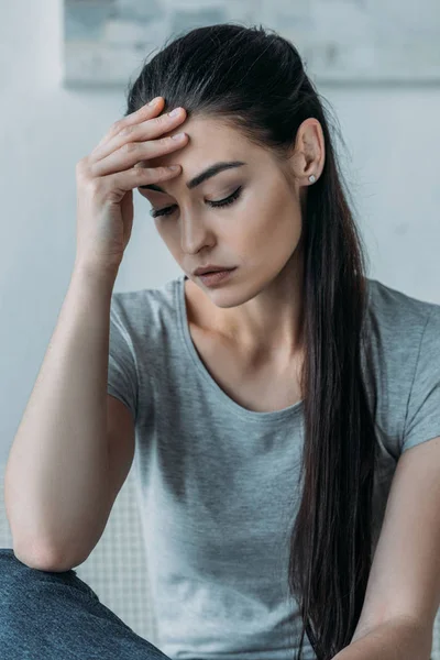 Portrait of sad young woman with hand on forehead looking down — Stock Photo