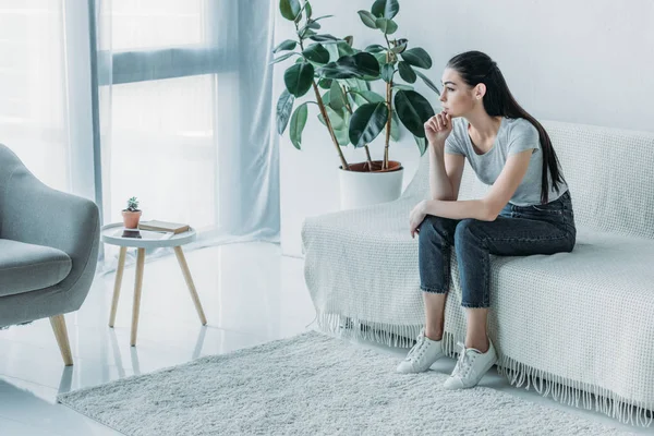 Высокий угол зрения грустной молодой женщины в депрессии, сидящей на диване и отводящей взгляд от дома — стоковое фото