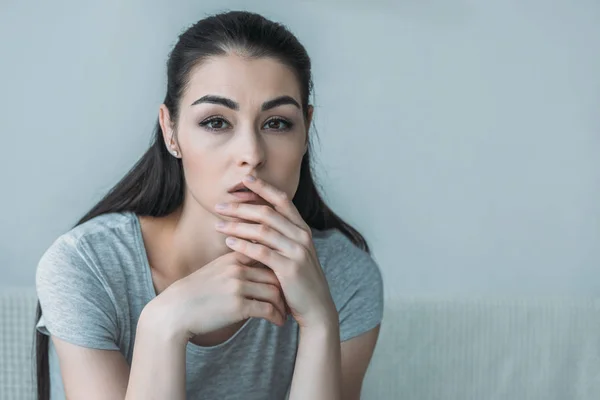 Portrait of depressed young woman sitting on couch and looking at camera — Stock Photo