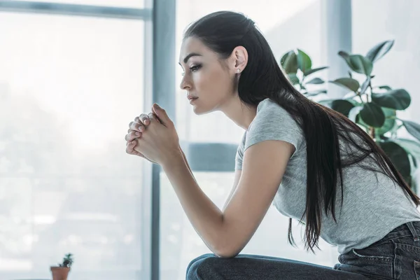 Side view of upset brunette woman sitting at home — Stock Photo